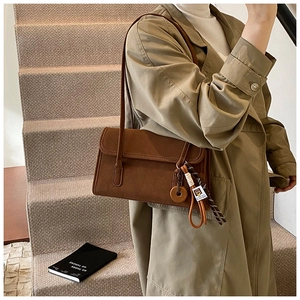 Detail of caramel brown frosted suede shoulder bag with decorative woven pendant