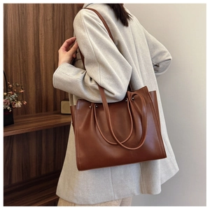 Side view of a vintage brown leather tote bag worn by a model in a cozy library setting