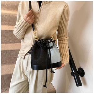 Detail of blue denim and black leather bucket bag with gold hardware and drawstring