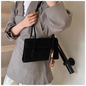 Detail shot of black matte suede underarm bag with decorative leather charm on a model