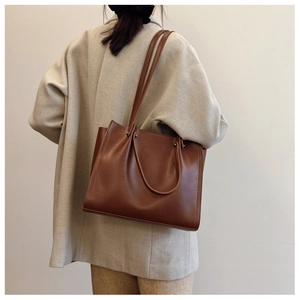 Close-up of a stylish brown leather tote bag worn with a chic beige blazer outfit