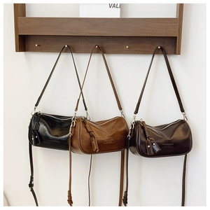 Trois sacs en cuir en noir, marron clair et marron foncé suspendus à un support en bois