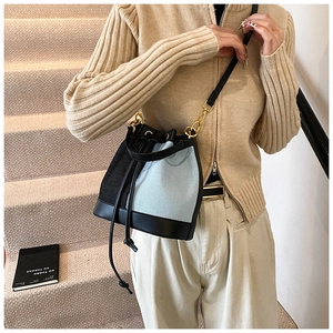 Close-up of a drawstring bucket bag with blue denim and black leather patchwork design