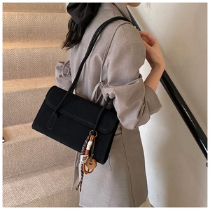 Detail of a matte black shoulder bag with rectangular flap and braided rope charm pendant