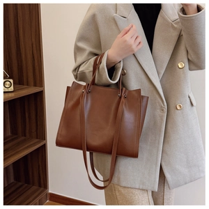 Detail view of brown leather tote bag with dual straps worn by model in beige blazer
