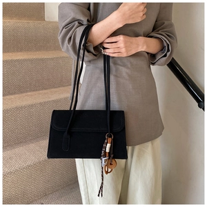 Detail of black suede underarm bag with silk scarf charm and stitching on rectangular flap