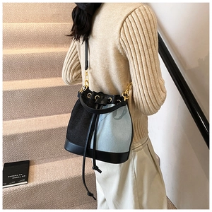 Detail of a color-block bucket bag with gold hardware and drawstring closure on a model