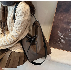 Brown bucket bag side view with bow detail on beige knitwear and pleated skirt