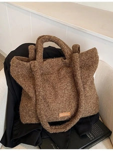 Brown fuzzy plush tote bag with wide straps displayed on a blazer and art book