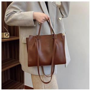Brown leather tote bag worn by a model in a beige suit for a chic minimalist fashion look