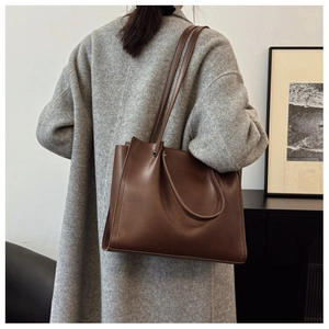 Detail of dark brown matte leather tote bag worn with a gray coat for a minimalist look