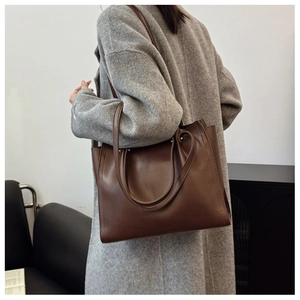 Detail view of large dark brown leather tote bag worn with a grey coat for commuting