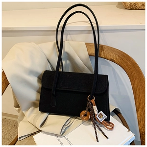 Detail of black frosted shoulder bag with decorative doughnut pendant on a wooden chair