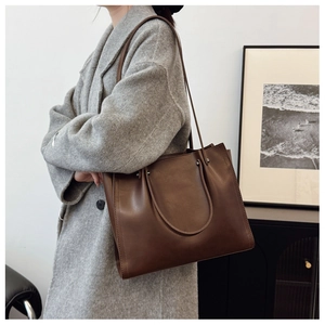 Detail of a large brown leather tote bag with fine stitching and slim shoulder straps