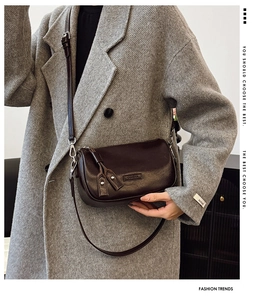 Détail du sac à bandoulière en cuir marron foncé avec pompon sur un manteau en laine