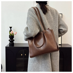 Detail of a large dark brown matte leather tote bag with dual straps on a model