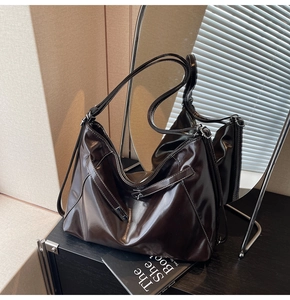 Detail of a large dark brown tote bag with high-gloss finish and soft hobo pleats
