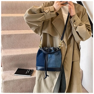 Detail of a drawstring bucket bag featuring blue denim and leather patchwork design