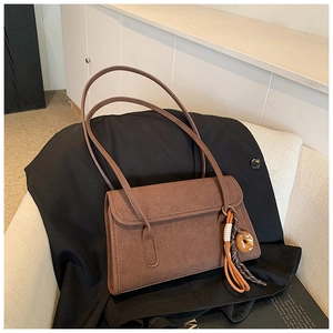 Close-up of brown suede shoulder bag with decorative marble ring and fringe tassel detail