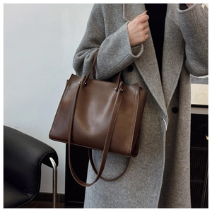 Brown leather tote bag featuring long handles and side gusset detail worn with a coat