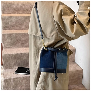 Detail of blue denim bucket bag with drawstring closure and golden hardware