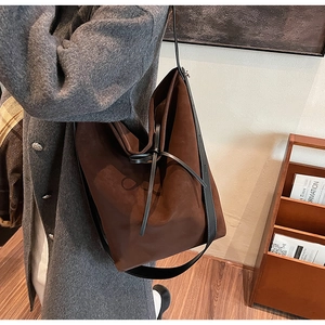 Brown suede tote bag detail with black leather straps shown in a stylish home setting