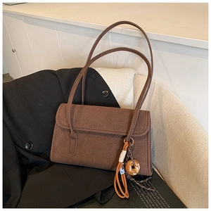 Detail of a brown frosted suede shoulder bag with a woven charm on a black blazer