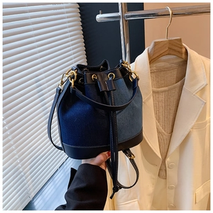 Detail of denim bucket bag with black leather trim and elegant gold hardware closure