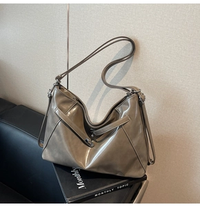 Detail of taupe tote bag with glossy finish and metal buckle against neutral wall