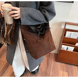 Gros plan d'un sac cabas en daim marron avec détail de bandoulière en cuir noué