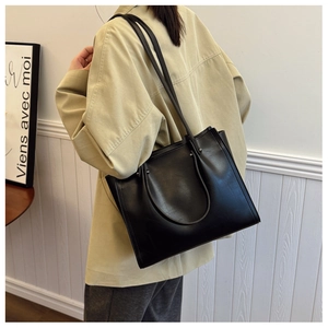 Detail of minimalist black leather tote bag with metallic stud accents on the shoulder strap