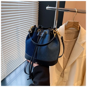 Detail of blue denim and black leather bucket bag with gold hardware and drawstring