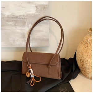 Detail of a brown suede shoulder bag featuring a woven knot and beaded tassel pendant