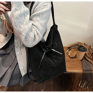 Detail of black suede tote bag featuring a decorative bow tie and soft matte texture