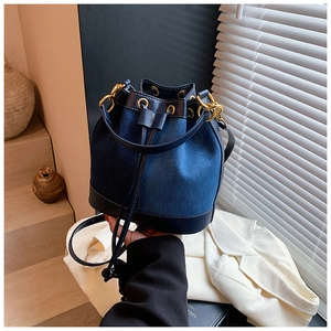 Detail of blue denim bucket bag with leather trim, gold hardware, and drawstring closure