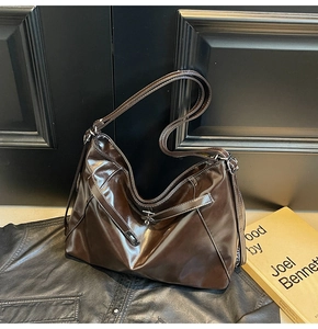 Détail du grand sac hobo café foncé au fini brillant sur fond de cuir noir élégant