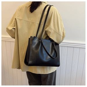 Side view of a large black minimalist tote bag worn by a model in a modern room