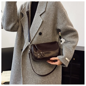 Détail du sac bandoulière en cuir marron foncé avec boucles sur manteau gris