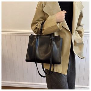 Detail view of a minimalist black tote bag in matte synthetic leather on a model's shoulder
