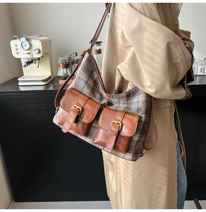 Brown plaid and leather shoulder bag with double buckles worn in a cafe setting