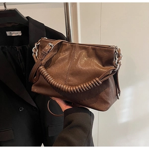 Dettaglio di una borsa a secchiello marrone con manico a spirale e fibbie argentate