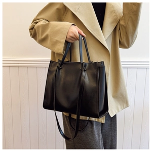 Fashionable black faux leather tote bag shown styled with a trench coat for daily casual wear