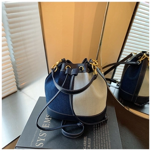 Detail of blue denim bucket bag with leather base and drawstring on mirror surface