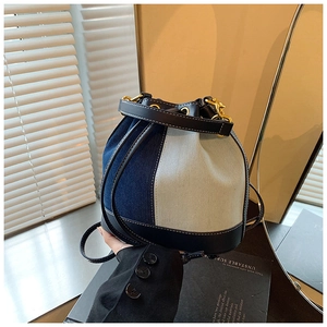 Detail of a color-block denim bucket bag with leather trim and contrast stitching