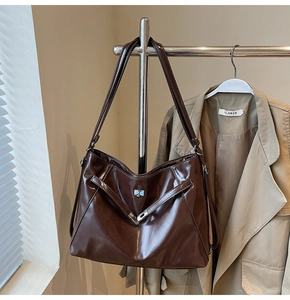 Detailed view of large coffee brown faux leather tote bag with metal buckle on a blazer