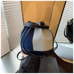 Detail of drawstring denim bucket bag with leather trim and gold metal hardware