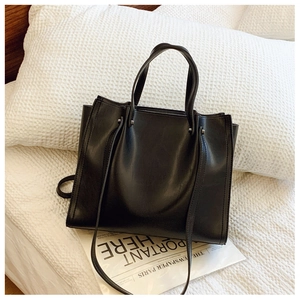 Detail of a matte black tote bag with silver studs and detachable strap on a bed