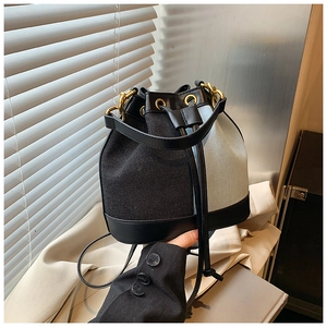 Detail of canvas bucket bag with black leather trim, drawstring and gold hardware