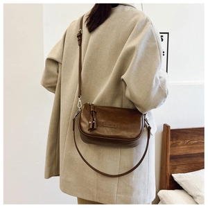 Sac bandoulière vintage marron foncé en cuir porté avec un manteau beige élégant et chic