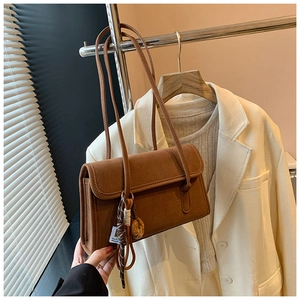 Detail of a brown matte suede shoulder bag with a decorative beaded charm and strap